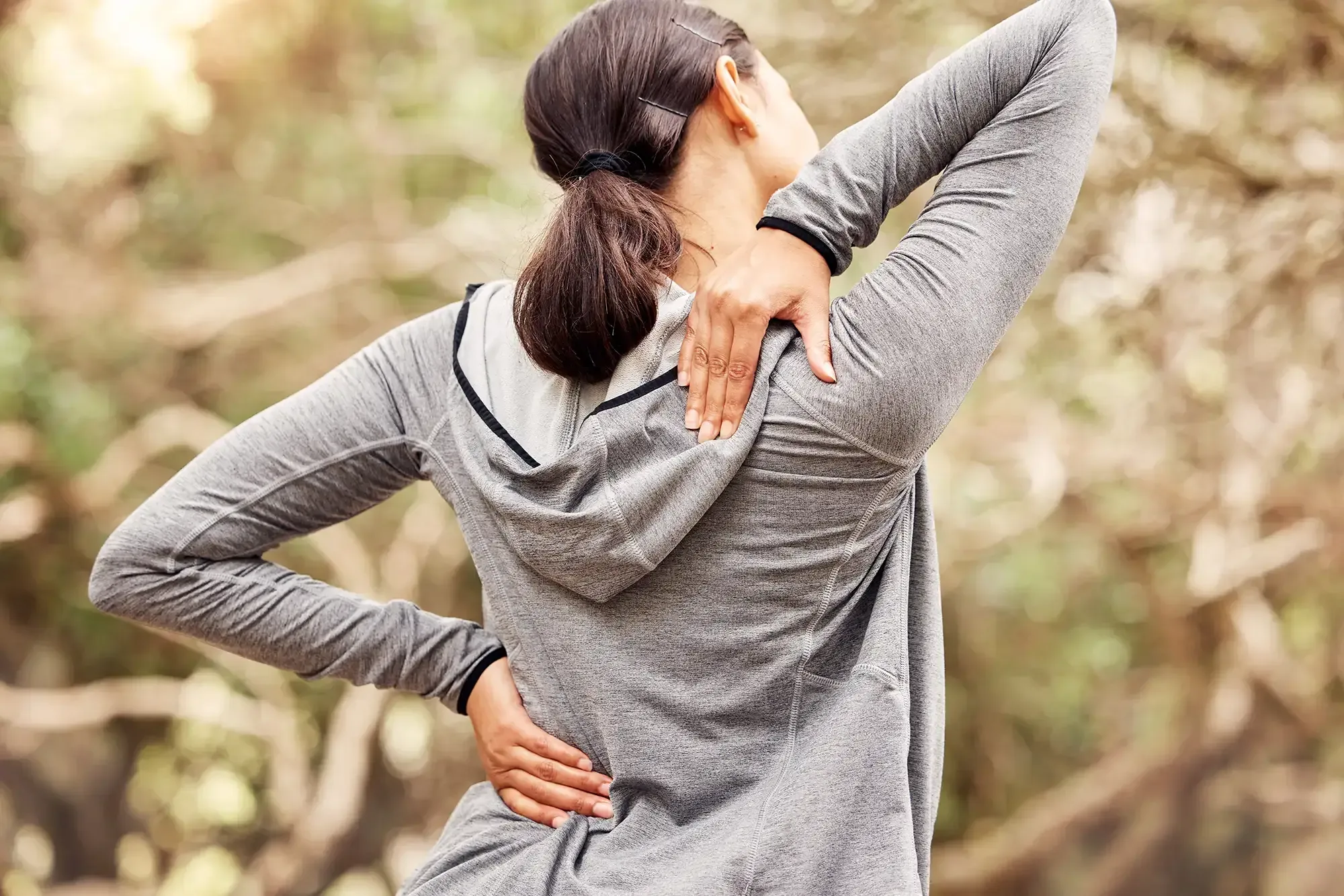 A woman in athletic wear holding her lower back while stretching outdoors