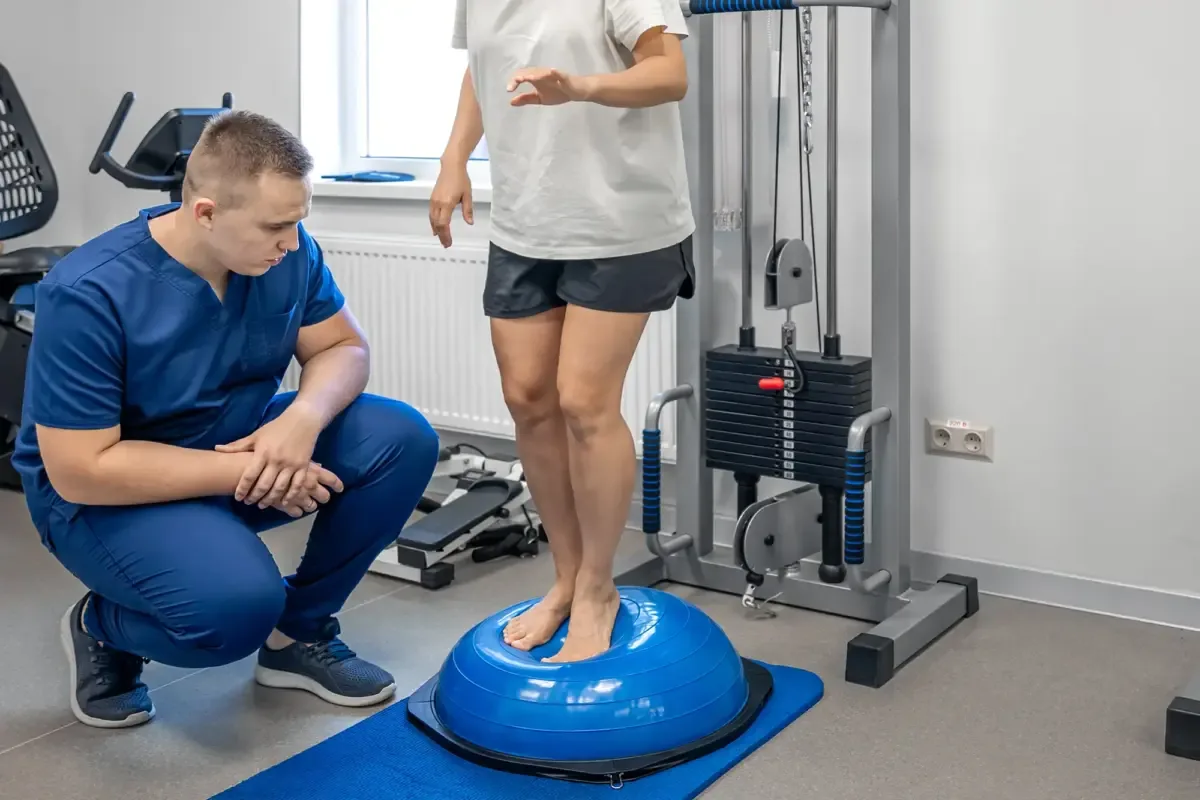 A clinician coaching a patient balancing on a bosu ball in a gym