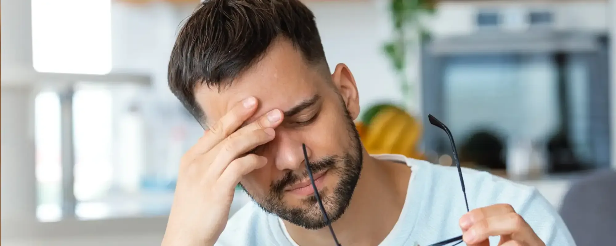 A man at a desk pressing his forehead, glasses in hand