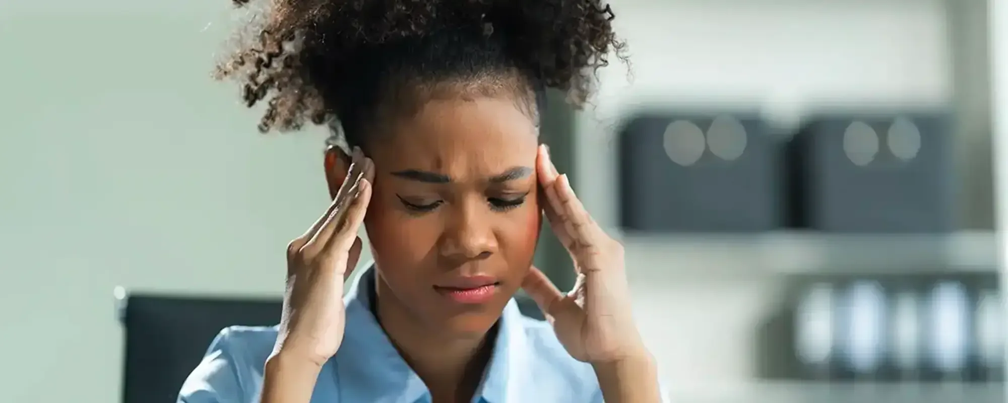 A woman at a desk pressing her temples during a headache