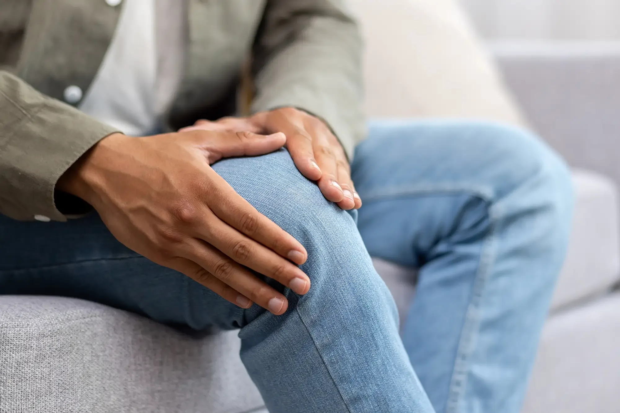 A close-up of a seated person&rsquo;s hands holding a painful knee