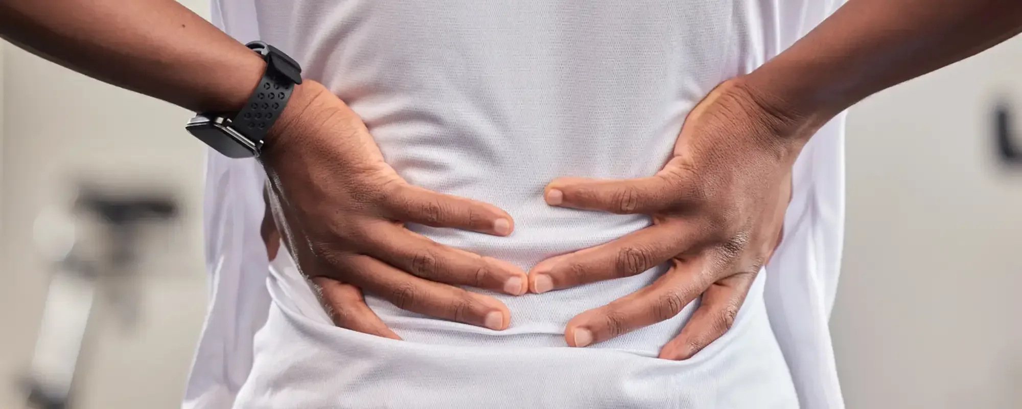 A person in a gym with both hands pressed to their lower back