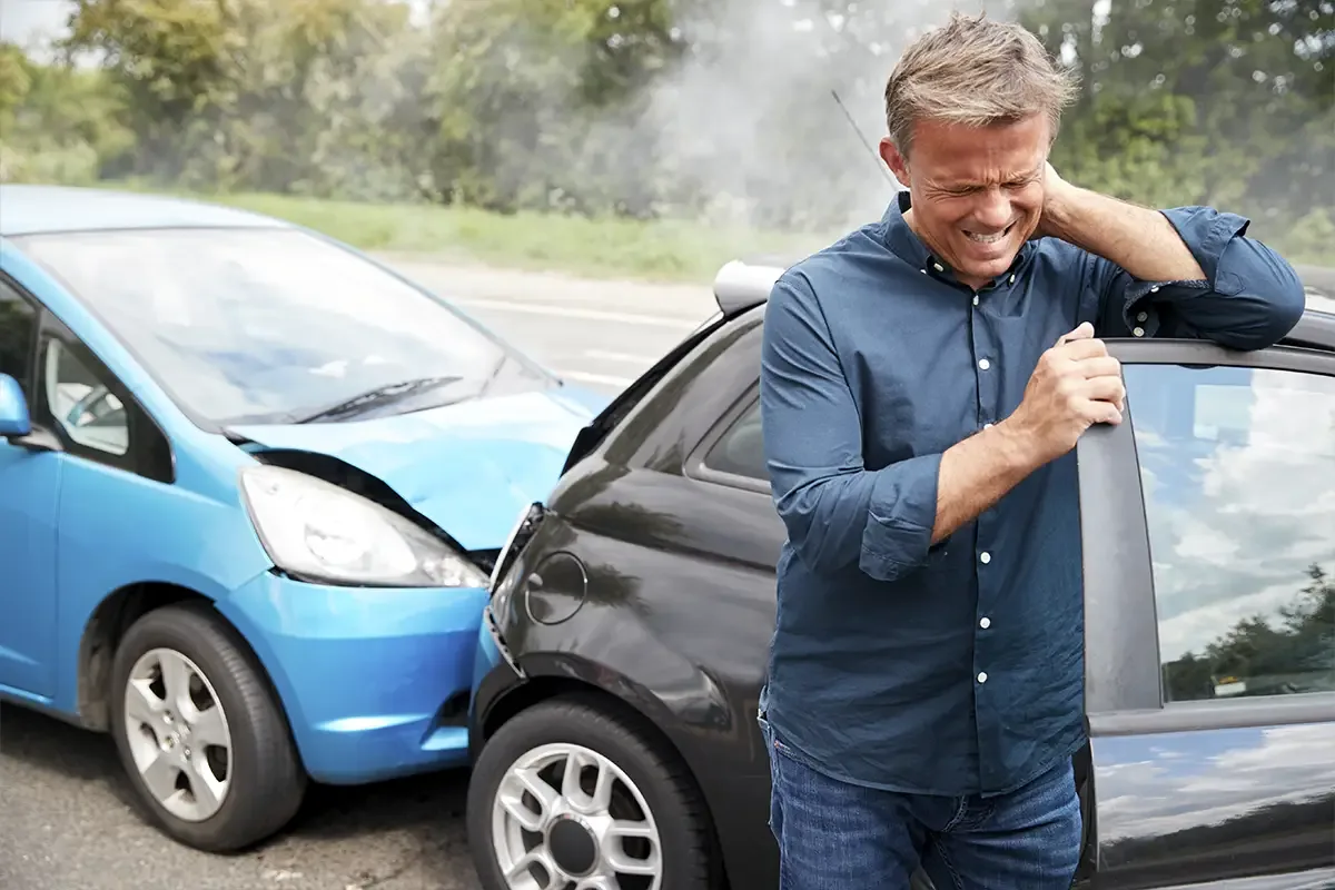 A man holding his neck beside two cars after a collision