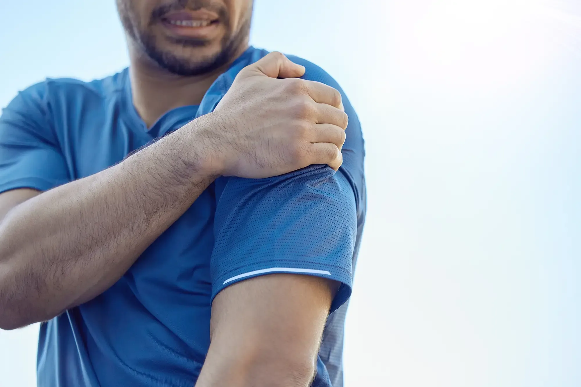 A man in a blue shirt gripping his shoulder in pain