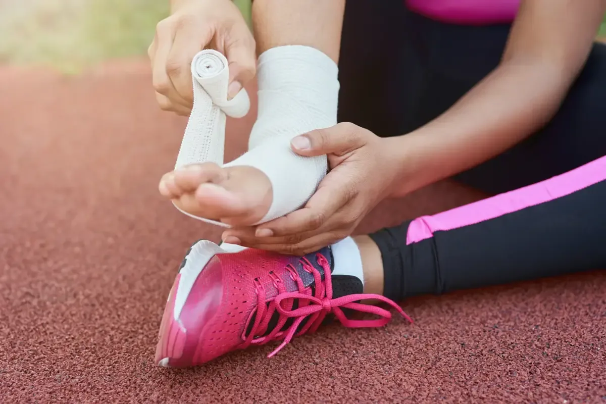 Hands wrapping an athlete&rsquo;s ankle with tape on a running track