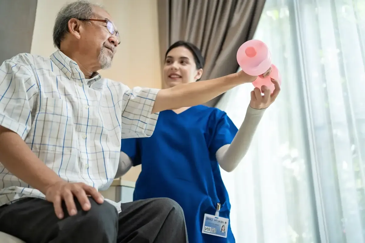 A clinician guiding a seated older man through a dumbbell exercise