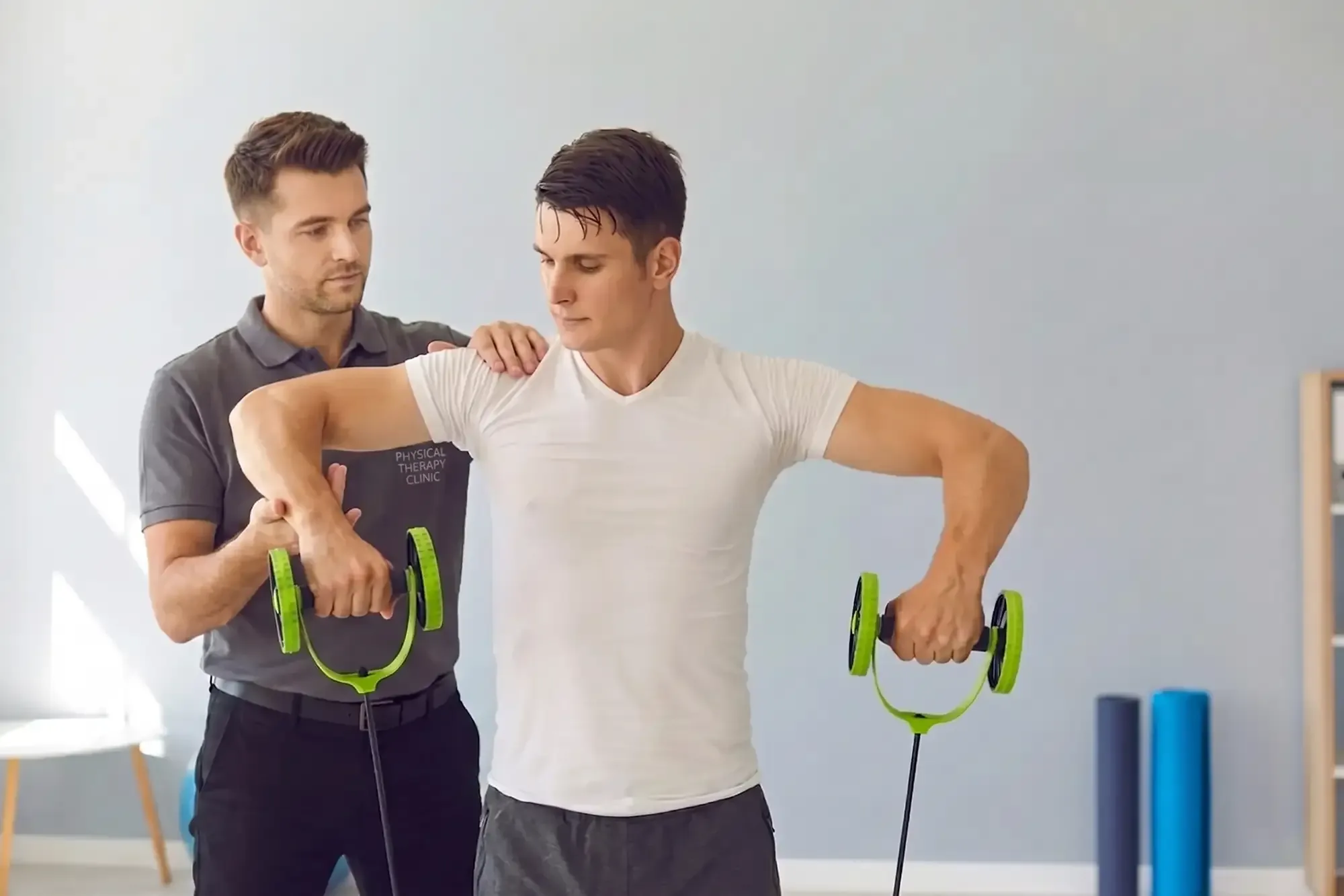 Therapist coaching an athlete pulling resistance handles overhead in a clinic gym