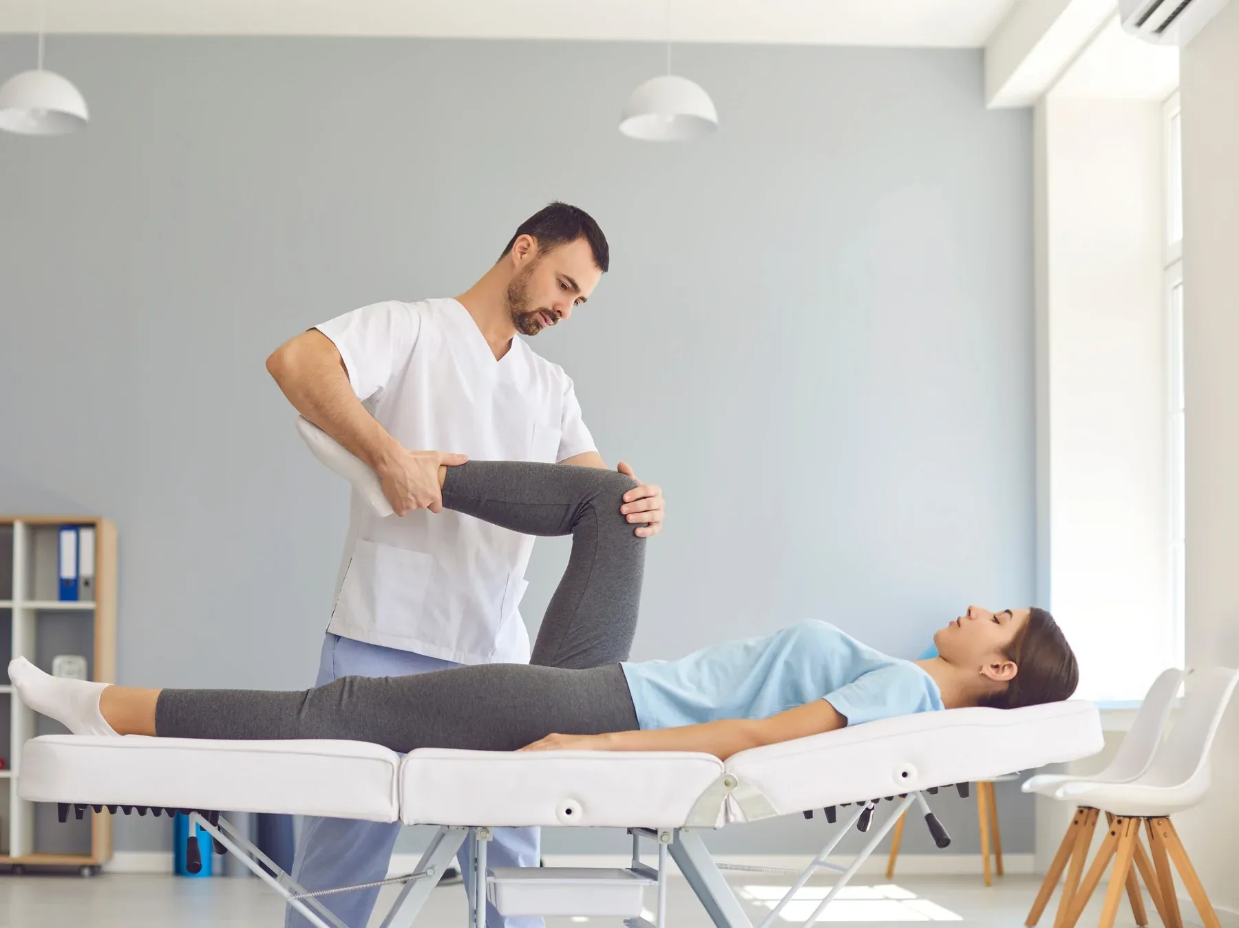 A therapist mobilizing the arm of a patient on a treatment table in a bright clinic